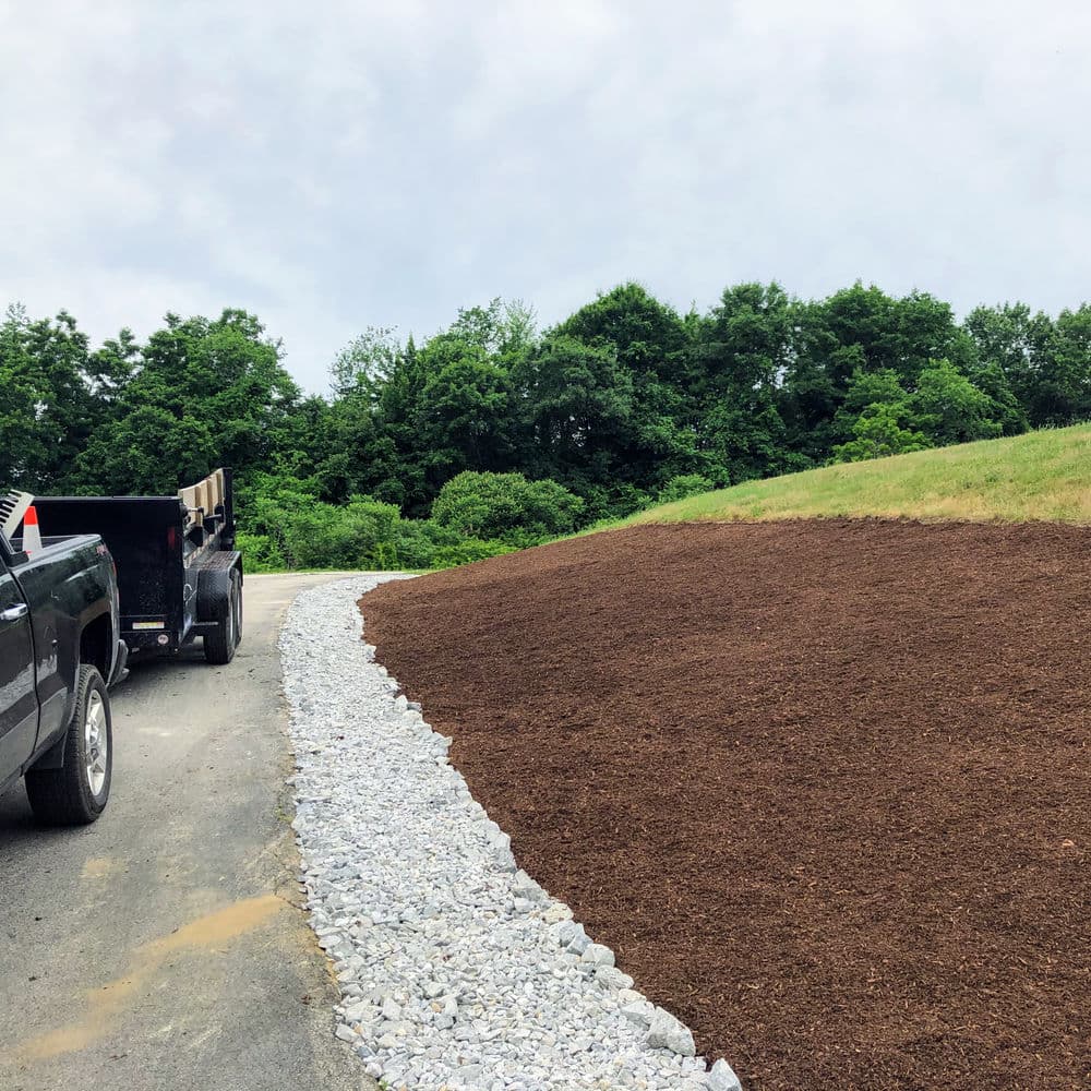 Landscape design featuring freshly mulched area and gravel pathway with trucks nearby.