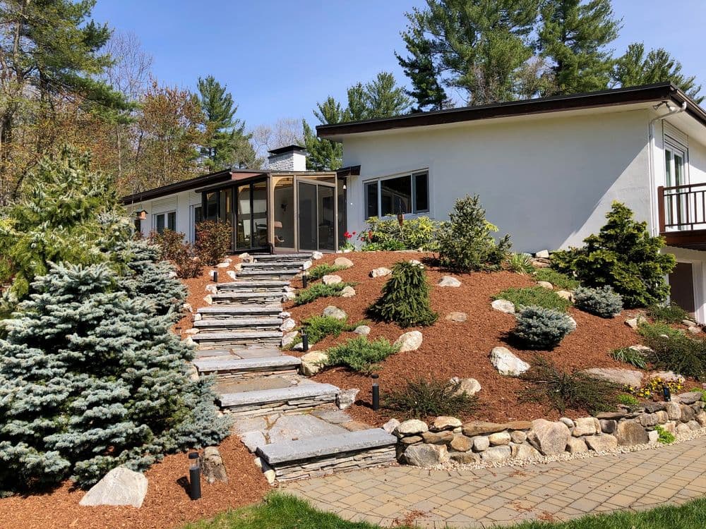 Modern home with landscaped garden, stone pathway, and vibrant greenery in bright daylight.